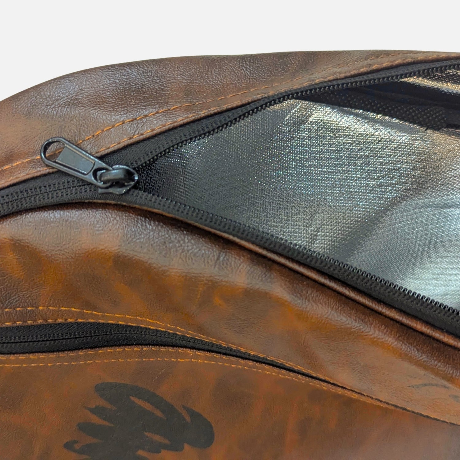 Close-up of a brown faux-leather bag with a black zipper and a black mesh pocket, showing a metallic silver interior lining. padel racket cover