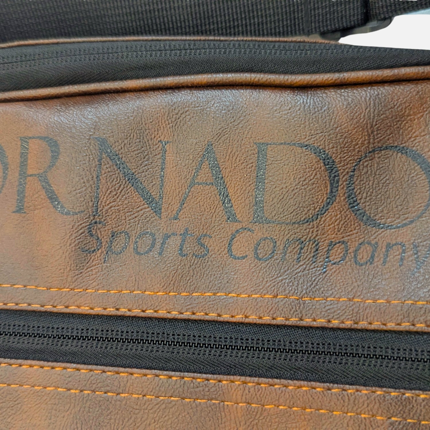 Close-up of a brown faux-leather bag or belt bag with black zippers and orange stitching, featuring the debossed text 'Padel tennis cover brown leather'.